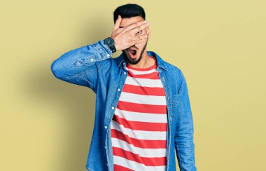 Sakallı, sıradan kot ceketli genç İspanyol bir adam. Şoka girmiş, yüzünü ve gözlerini kapamış, utangaç ifadesiyle parmaklarının arasından bakıyor.. 