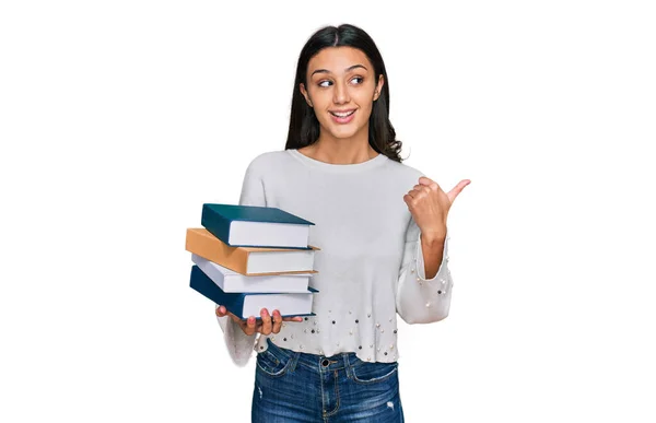 Jovencita Hispana Sosteniendo Montón Libros Apuntando Con Pulgar Hacia Costado — Foto de Stock