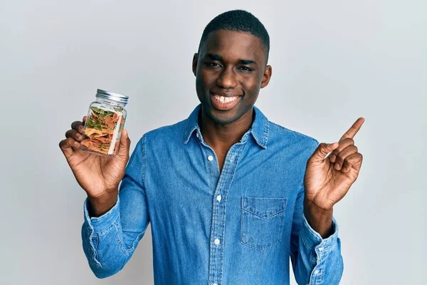 Joven Hombre Afroamericano Sosteniendo Frasco Con Pasta Farfalle Sonriendo Feliz — Foto de Stock