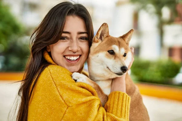 Güzel genç bir kadın parkta mutlu Shiba Inu köpeğine sarılıyor.