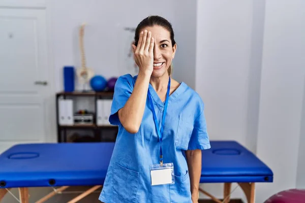 Młoda Latynoska Kobieta Mundurze Fizjoterapeuty Stojąca Klinice Zakrywającej Jedno Oko — Zdjęcie stockowe