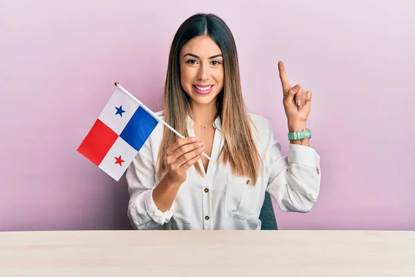 テーブルの上に座っているパナマの旗を持っている若いヒスパニック系の女性幸せな顔をしたアイデアや質問指差す指で笑顔 ナンバーワン — ストック写真