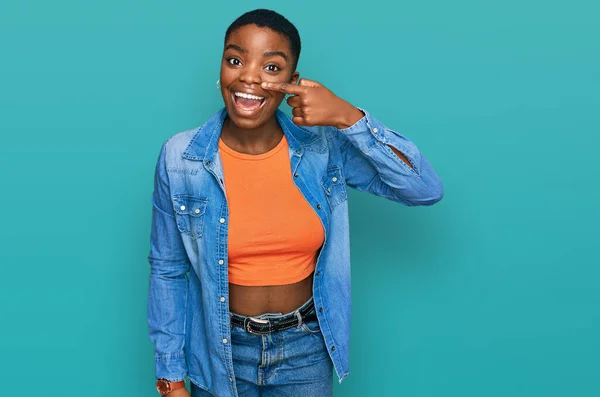 若いアフリカ系アメリカ人の女性は 顔や鼻に手指で指してカジュアルな服を着て 陽気に笑っています 美の概念 — ストック写真