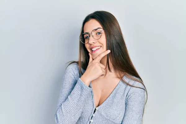 カジュアルなセーターと眼鏡を身に着けている若いブルネットのティーンエイジャーは カメラが交差した腕と手で笑みを浮かべていることに自信を持っている ポジティブな — ストック写真