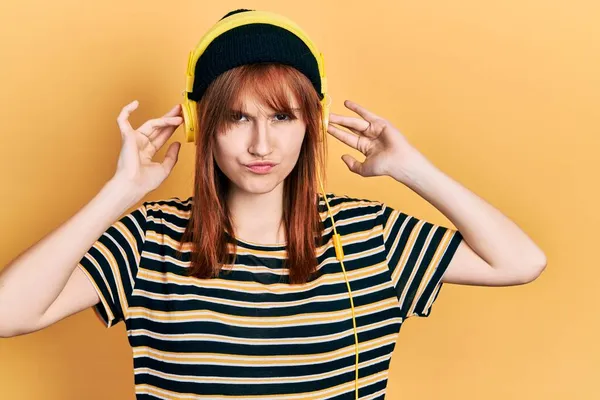 Kızıl saçlı genç kadın, kulaklık takıyor şüpheci ve gergin, sorun yüzünden surat asıyor. negatif kişi. 