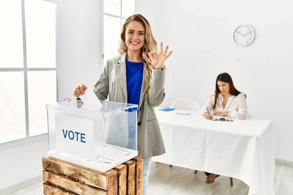 Joven Mujer Rubia Votando Poniendo Sobre Las Urnas Haciendo Signo —  Fotos de Stock