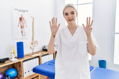 Ağrı kesici kliniğinde çalışan beyaz bir kadın dokuz numarayı gösterip işaret ederken kendinden emin ve mutlu bir şekilde gülümsüyor.. 