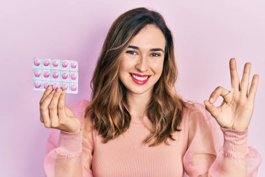 Genç İspanyol kız elinde haplar tutuyor. Parmaklarıyla imza atıyor. Gülümsüyor. 