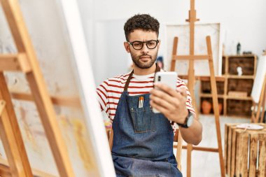 Sanat stüdyosunda akıllı telefon çizimi yapan genç bir Arap sanatçı..