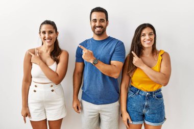 Bir grup İspanyol genç, izole edilmiş arka planda mutlu bir şekilde ayakta duruyor. Yüzlerinde gülücükler, mutlu ve doğal bir ifadeyle elleri ve parmaklarıyla yüzünü gösteriyorlar. 
