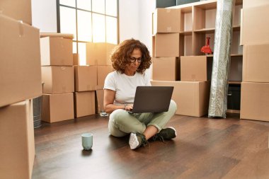 Orta yaşlı İspanyol bir kadın dizüstü bilgisayarla yerde oturuyor. Tavırları düşünüyor ve kendine güveniyor gibi görünüyor. 