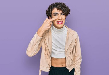 Handsome man wearing make up and woman clothes pointing with hand finger to face and nose, smiling cheerful. beauty concept 