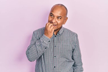 Orta yaşlı, sıradan kıyafetler giyen, stresli ve gergin görünen, elleri ağızdan tırnak yiyen Latin bir adam. anksiyete. 