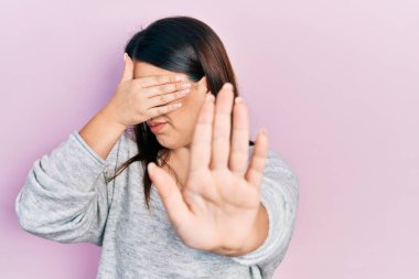 Elleriyle gözlerini kapatan, üzgün ve korku ifadeleriyle jestler yapan Latin asıllı genç bir kadın. utangaç ve olumsuz kavram. 