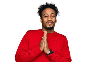 Sakallı, kışlık süveter giyen, elleri bağlı dua eden, affedilmek isteyen, kendinden emin gülümseyen Afro-Amerikalı genç bir adam.. 