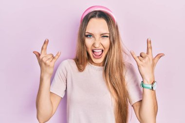 Sıradan kıyafetler giyen, çılgın bir ifadeyle bağıran genç sarışın kız elleri havada rock sembolü yapıyor. Müzik yıldızı. ağır müzik konsepti. 