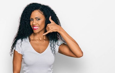 Orta yaşlı Afro-Amerikalı kadın, günlük beyaz tişörtler giyip gülümsüyor, telefonla el ve parmak hareketleri yapıyor, telefonda konuşuyor gibi. iletişim kavramları. 