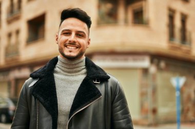 Genç Arap adam gülümsüyor, mutlu bir şekilde şehirde duruyor..