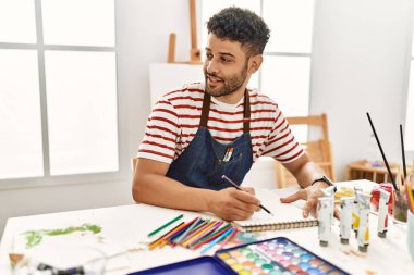 Sanat stüdyosunda gülümseyen genç Arap ressam mutlu çizimler yapıyor..