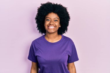 Genç Afro-Amerikalı kadın günlük kıyafetler giyiyor. Pozitif ve mutlu görünüyor. Kendine güvenen bir gülümsemeyle dişlerini gösteriyor. 