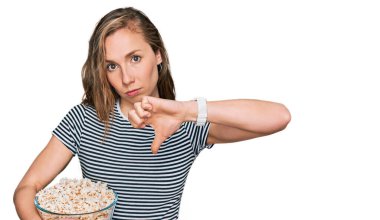 Kızgın yüzle patlamış mısır yiyen genç sarışın kadın, olumsuz işaret baş parmakları aşağıda, reddedilme konsepti 