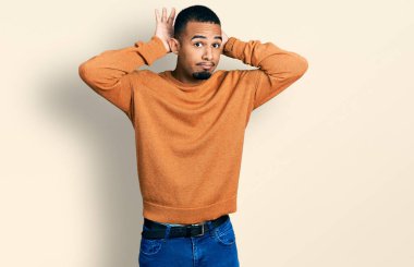 Genç Afro-Amerikan adam günlük kıyafetler giyiyor tavşan kulağı yapıyor avuç içi hareketleriyle kuşkucu ve şüpheci görünüyor. Paskalya tavşanı konsepti. 