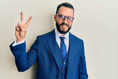 Sakallı, takım elbiseli ve kravatlı genç adam iki numaralı parmaklarını gösterip gösterirken kendinden emin ve mutlu gülümsüyor.. 