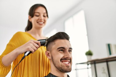 Genç İspanyol kuaför kadın güzellik merkezinde tıraş makinesi kullanarak adamın saçını kesiyor..