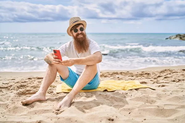 Genç Kızıl Saçlı Adam Kumsalda Havluya Oturmuş Akıllı Telefon Kullanıyor — Stok fotoğraf