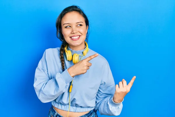 若いヒスパニック系の女の子は ヘッドフォンを使用して音楽を聞いて笑顔とカメラを見て2本の手と指で側面を指して — ストック写真