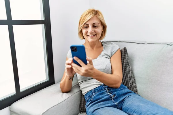 Mujer Rubia Mediana Edad Sonriendo Confiada Usando Teléfono Inteligente Casa — Foto de Stock