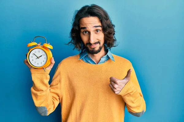 目覚まし時計を持っている若いヒスパニック系の男が笑顔と正 親指アップ行う優れた承認サイン — ストック写真