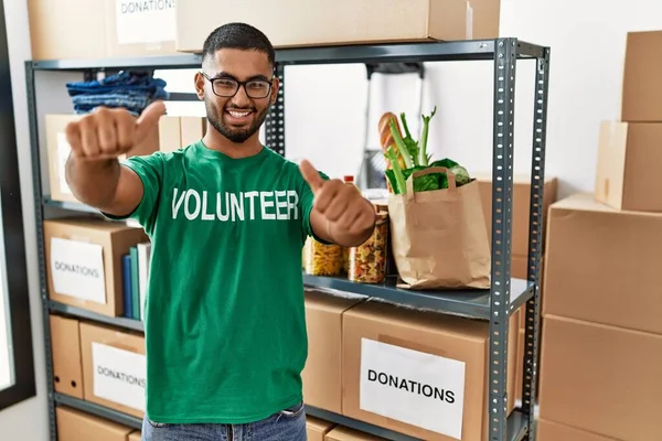 寄付箱を持っている若いインドの男性ボランティアは 手で積極的なジェスチャーを行うことを承認します 親指アップ笑顔と成功のために幸せ 勝者のジェスチャー — ストック写真