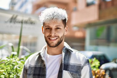 Genç İspanyol adam gülümseyerek şehirde mutlu mesut dikiliyor..