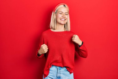 Güzel sarışın kadın gündelik kırmızı süveter giyiyor. Çok mutlu ve heyecanlı. Kazanan bir jest yapıyor. kutlama konsepti. 
