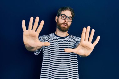 Sakallı, çizgili tişörtlü, gözlüklü, korkudan dehşete düşmüş beyaz bir adam. panik konsepti. 