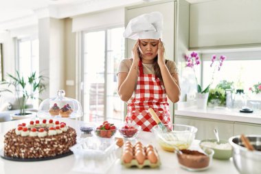 Güzel, genç, esmer pasta şefi kadın stres yüzünden elleri başının üstünde pasta pişiriyor. migren ağrısı. 