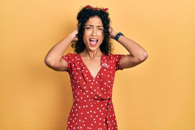 Yazlık elbise giyen genç Latin kız çılgın ve elleri başında korkmuş, şokdan korkmuş ve ağzı açık. 