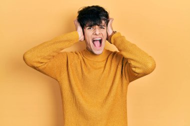 Yakışıklı hippi genç adam gündelik sarı süveter giyiyor çılgın ve elleri kafasında korkmuş, korkmuş ve ağzı açık şoktan şaşırmış. 