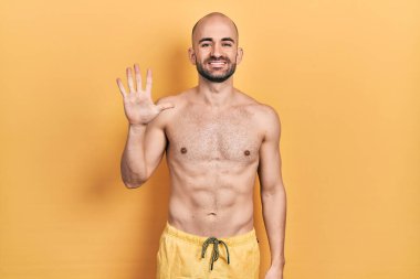 Mayo giyen genç kel adam gülümseyerek mutlu ve kendinden emin gülümserken beş numarayı gösteriyor ve işaret ediyor.. 