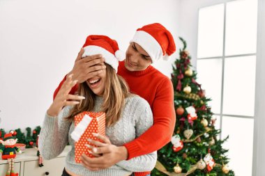 Genç çift sarılıyor ve gülümsüyor. Evde hediyeli bir erkek, kadını şaşırtıyor..