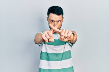 Gündelik kıyafetler giyen genç İspanyol adam reddedilme ifadesini negatif işaret yaparak parmaklarını çapraz yapıyor. 