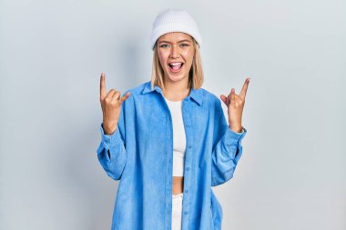 Yün şapkalı güzel sarışın kadın çılgın bir ifadeyle bağırıyor ve elleri havada rock sembolü yapıyor. Müzik yıldızı. ağır müzik konsepti. 