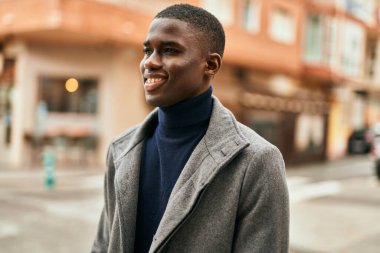 Genç Afrikalı Amerikalı adam gülümseyerek şehirde mutlu mesut duruyor.