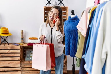 Genç İspanyol kadın elbise mağazasında akıllı telefondan konuşuyor.