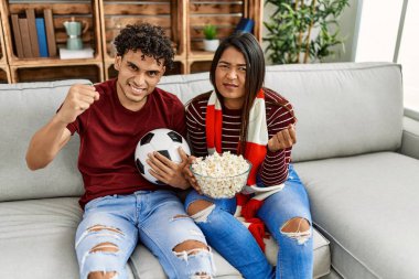 Evdeki kanepede oturan genç latin çift futbol maçını izliyor ve destekliyor..