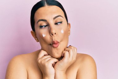 Güzel esmer kadın, üstsüz, yüz kremi sürmüş, balık suratlı, şaşı gözlü, çılgın ve komik.. 