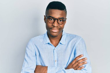 Sıradan kıyafetler ve gözlük takan, kollarını kavuşturup kameraya gülümseyen genç Afro-Amerikan bir adam. pozitif kişi. 