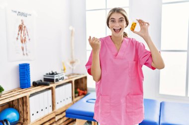 Ağrı kesici kliniğinde çalışan genç fizyoterapist kadın elinde haplarla gururla bağırıyor zaferi ve başarıyı kutluyor. 