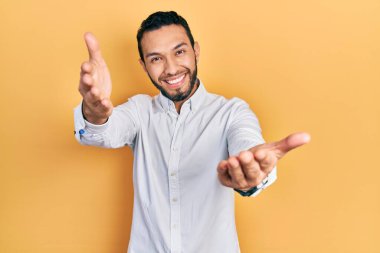 Sakallı, iş gömleği giyen, kameraya bakıp kucaklaşmak için gülümseyen İspanyol bir adam. Mutluluğu kucaklayan neşeli bir ifade.. 